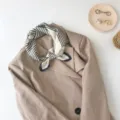 Elegant black and white striped silk square scarf styled on a chic beige blazer detail view. - White
