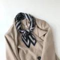 Close-up detail of a black and white pleated geometric scarf styled on a chic beige blazer. - Greek Key Grey
