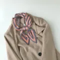Detailed view of pleated geometric pattern small square scarf tied neatly on chic blazer. - Greek Key Pink