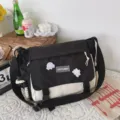 Detailed shot of black and white canvas messenger bag with flap closure and cute cartoon pins. - No Pendant / Black