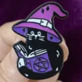 Close-up detail of a cute gothic black cat enamel pin wearing a purple witch hat reading book. - Witch Hat Cat