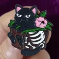 Close-up detail shot of a cute dark style black cat enamel pin with skeleton bones and flower. - Floral Skeleton Cat