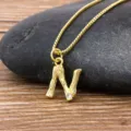 Minimalist gold plated letter N pendant necklace with sparkling stone detail on dark stone. - Letter N