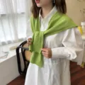 Vista detallada de un elegante chal de punto verde anudado sobre una camisa blanca. - Aguacate