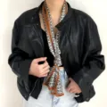 Dettaglio di un foulard in seta stretto con stampa geometrica indossato con giacca di pelle. - J109