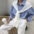 Vue détaillée d'une chemise rayée bleue avec un pull en tricot blanc posé sur les épaules. - Blanc Lait