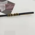 Close-up detail showing the exquisite antique brass rose metal buckle on a sleek black waist belt. - Black
