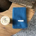 Detailaufnahme eines blauen Strickschals mit feiner Rippenstruktur und weißem Label. - Klein-Blau