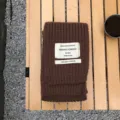 Nahaufnahme des braunen Strickschals mit stilvollem Stoffetikett auf Holztisch und Kies. - Braun