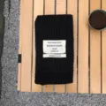 Detailaufnahme eines schwarzen Strickschals mit gewebtem Etikett auf Holztisch platziert. - Schwarz