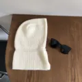 Detailed view of a cozy white knitted balaclava winter hood scarf, soft texture on wooden table. - One Size / Milk White