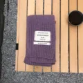 Nahaufnahme eines violetten, gestrickten Winterschals mit aufgenähtem Textiletikett. - Lila