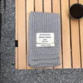 Grauer Strickschal im Detail, weiches kuscheliges Wollmaterial mit dekorativem Weblabel. - Hellgrau