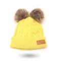 Close-up of yellow kids knit beanie detail, featuring fluffy faux fur pom poms and leather tag. - One Size / Yellow