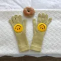 Nahaufnahme Detail der kuscheligen Strick-Winterhandschuhe mit süßem Smiley-Aufnäher. - Erdgelb