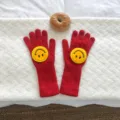 Nahaufnahme von roten Strickhandschuhen mit süßem gelben Smiley-Gesicht für den Winter. - Rot