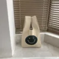 Beigefarbene Strick Handtasche mit niedlichem schwarzen Smiley Gesicht Design für Alltag. - Gebrochenes Weiß