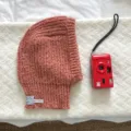 Close-up of pink knitted balaclava hood with warm fleece texture and brand label. - 24x31cm / Coral