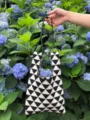 Vista di dettaglio della borsa tote in maglia geometrica bianco e nero tra ortensie blu. - Stile Tracolla in Pelle PU / Nero