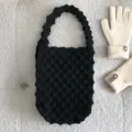 Close-up van zwarte gebreide handtas met gewolfde handgreep op zachte witte achtergrond. - Zwart