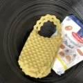 Detailopname van een gele mini gebreide handtas met popcorntextuur op een zwart bord. - Mosterdgeel