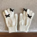 Detailaufnahme süßer Strickhandschuhe in Cremeweiß mit verspielten schwarzen Schleifen. - 21x11cm-U203S / Weiß