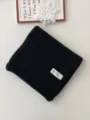 Nahaufnahme eines ordentlich gefalteten schwarzen Strickschals mit handgemachtem Label. - 170x22cm / Schwarz