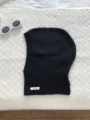 Detail view of black 100% wool balaclava knit hood, featuring a wool label and soft texture. - Black