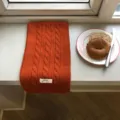 Detailansicht des gemütlichen orangen Zopfmuster-Winterschals auf heller Fensterbank. - 150x20cm / Orangerot