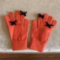 Nahaufnahme oranger Strickhandschuhe mit schicken schwarzen Schleifen an den Fingern. - 21x11cm-U203S / Orange