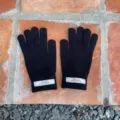 Detailaufnahme schwarzer Strickfünffingerhandschuhe mit weißem Markenetikett am Bündchen. - 21x11cm-H005S / Schwarz