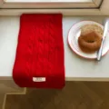 Detailansicht eines weichen roten Zopfmuster-Winterschals auf einer weißen Fensterbank. - 150x20cm / Rot