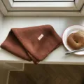 Gemütlicher brauner Strickschal in warmer Detailansicht auf einer weißen Fensterszene. - 160x21cm / Karamellbraun