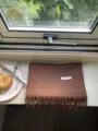 Close-up detail of a solid brown wool scarf with fringe laid on a windowsill with a plate. - Coffee