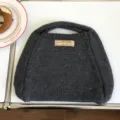 Nahaufnahme der dunkelgrauen Strickhandtasche auf weißem Tisch mit feiner Wolltextur. - 31x26cm / Grau
