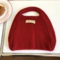 Detailansicht einer roten Strickhandtasche mit strukturiertem Wollstrick und gewebtem Etikett. - 31x26cm / Rot