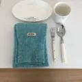 Detailaufnahme eines gemütlichen blau-grünen Strickschals mit Etikett im minimalistischen Stil. - Hellblau