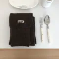 Detailansicht eines kuscheligen dunkelbraunen Strickschals mit gewebtem Etikett, flachgelegt. - Dunkelbraun
