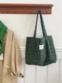 Detailed view of green plaid wool tote bag hanging in cozy lifestyle scene with autumn coat. - Green