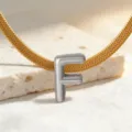 Nahaufnahme Detail eines silbernen Buchstaben F Anhängers an goldener Schlangenkette. - Halskette F