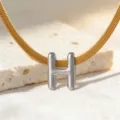 Detailaufnahme des silbernen Buchstaben-H-Anhängers an einer goldenen flachen Schlangenkette. - Halskette H