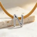 Nahaufnahme Detail des silbernen gepufften Buchstaben N Anhängers an goldener flacher Schlangenkette. - Halskette N