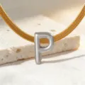 Detailansicht einer goldenen Schlangenkette mit silbernem Buchstaben P Anhänger auf Stein. - Halskette P