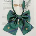 Detail shot of green plaid JK uniform bow tie with navy stripes and gold crest embroidery. - 009-LJ