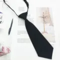 Close-up detail of a solid black kids short necktie with adjustable strap, flat lay on paper. - Black
