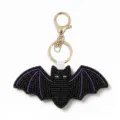 Bead bat keychain detail showing intricate black and purple seed bead embroidery and gold hardware. - Bat
