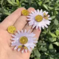 Nahaufnahme der handgemachten Acryl Ohrringe mit lila Gänseblümchen und glitzernden Bienen. - Lila Bienen- und Gänseblümchen-Ohrringe