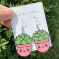 Detailaufnahme niedlicher Topfpflanzen Acryl Ohrringe mit grünem Kaktus Design auf der Karte. - Rosa Topfpflanzen-Ohrringe