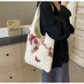 Close-up detail of the beige canvas tote bag featuring delicate red lace embroidery. - Red