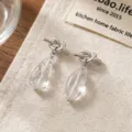 Primo piano dettagliato di orecchini nodo argento con ciondoli a goccia trasparenti. - Stile Nodo